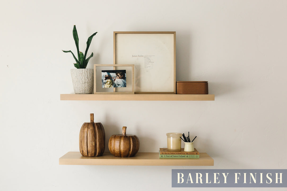 A basswood floating shelf with a barley finish applied decorated with books, pumpkin props, photo frame, aroma sticks, a candle, and a plant arranged on it, set against a white wall
