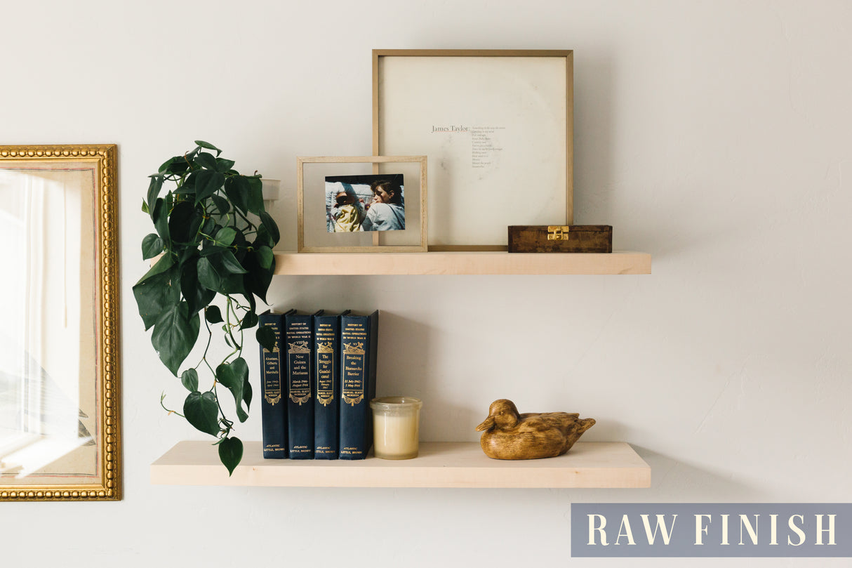 A basswood floating shelf with a no finish applied decorated with books, a wooden mallard, photo frames, and a plant arranged on it, set against a white wall