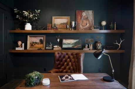 A dark home office with a brown leather chair and warm wood floating shelves