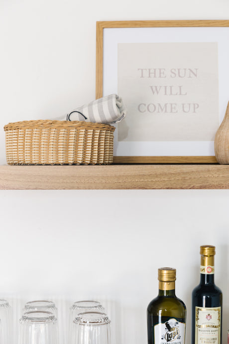 Walnut floating shelves with the bleached finish applied decorated with glass cups, oils, wooden basket with towel, photo frame, and a wooden vase